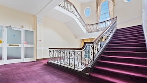 A grand staircase with a purple carpet and ornate black railings, leading to a reception area with frosted glass doors and a blue circular window. - Compact Studios in Dudley (Dudley)