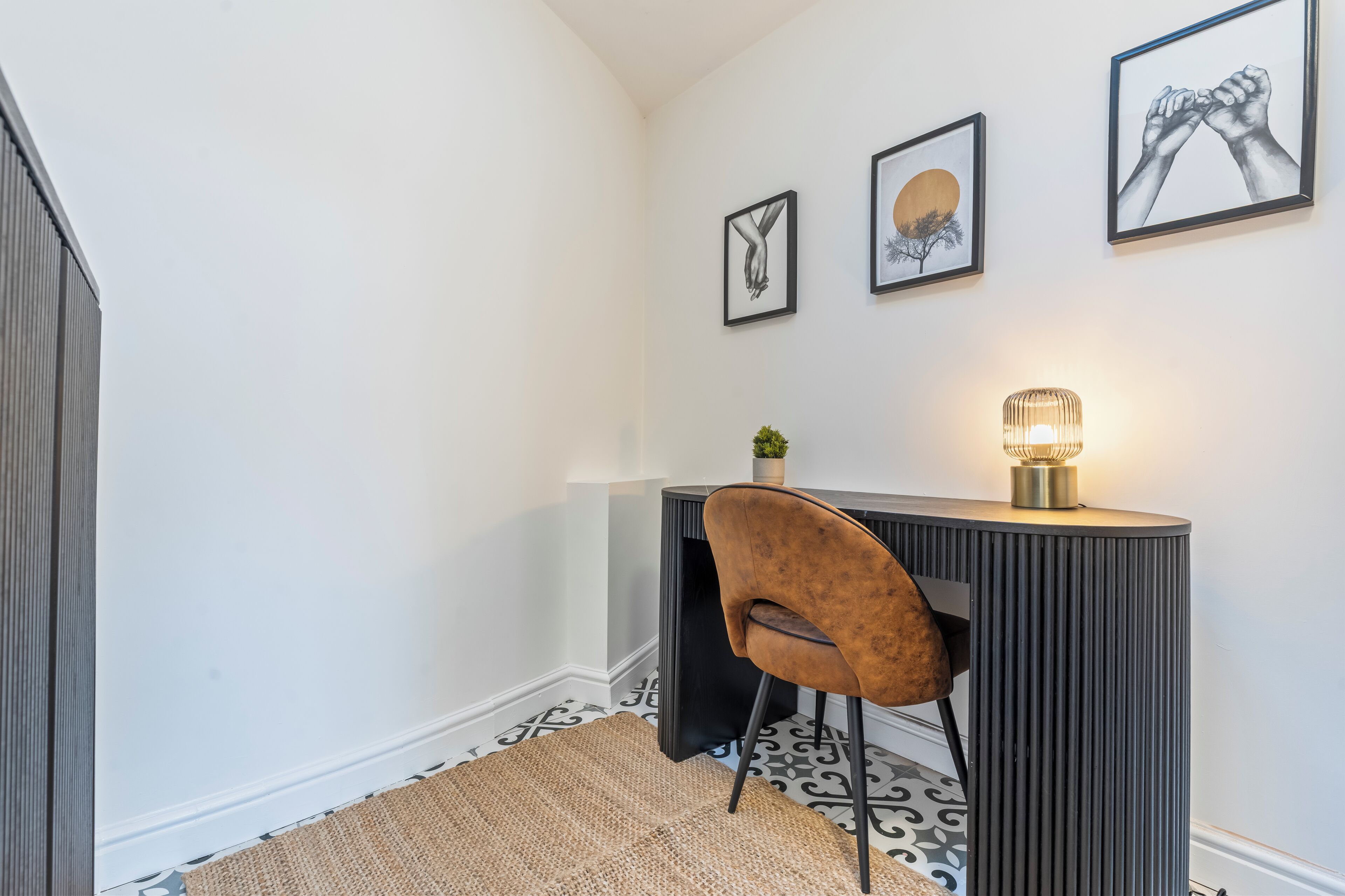 A corner room with a desk, chair, and wall-mounted lamp.