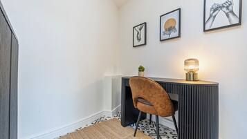 A corner room with a desk, chair, and wall-mounted lamp.