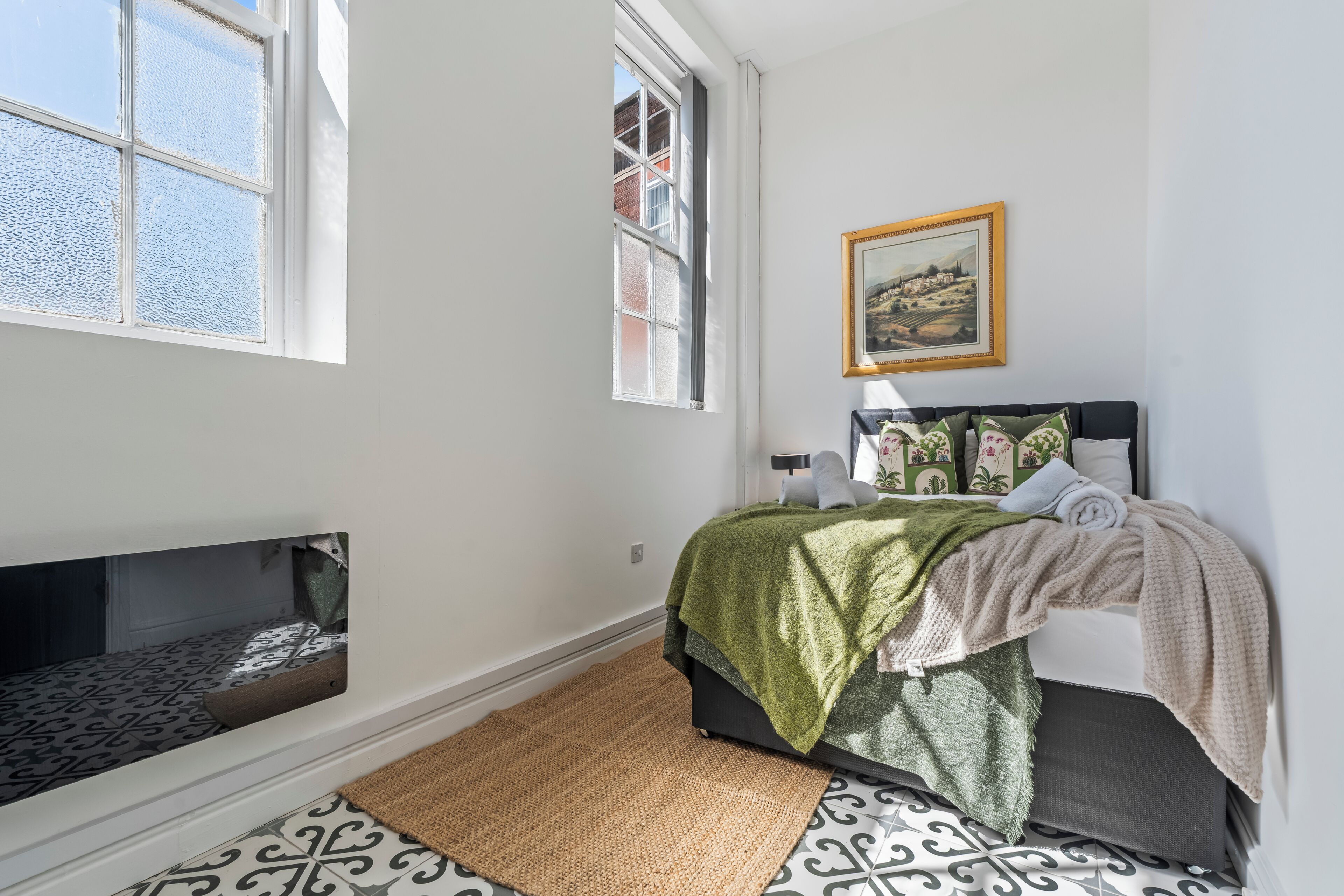 A bedroom with a bed, a window, a painting, and a built-in bench.