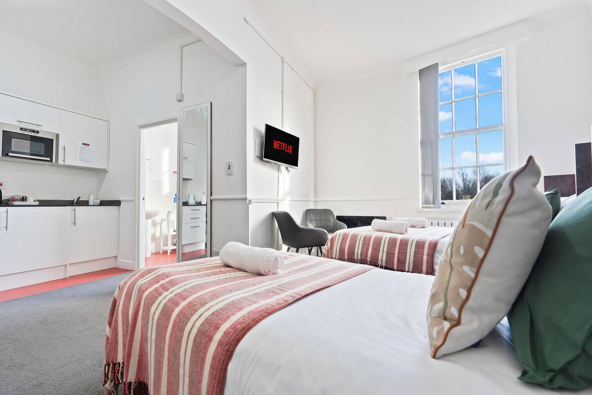A modern hotel room with a bed, a TV, a desk, and a view of the outdoors.