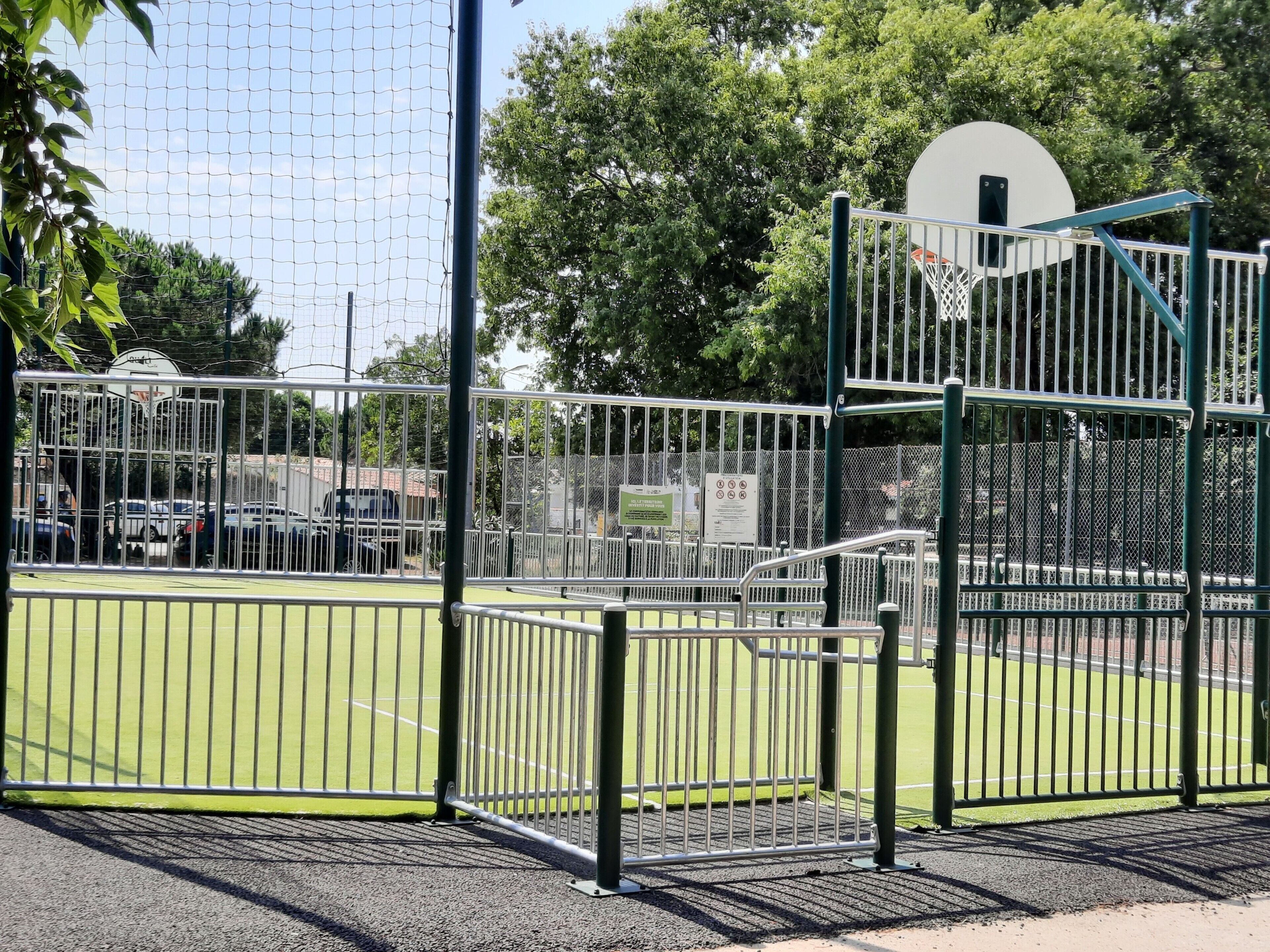 Una cancha deportiva con un aro de baloncesto, rodeada de vallas metálicas y árboles.