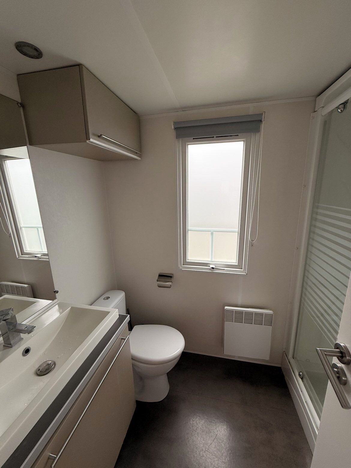 Une petite salle de bain comprenant des toilettes, un lavabo, un miroir, une fenêtre et une douche.