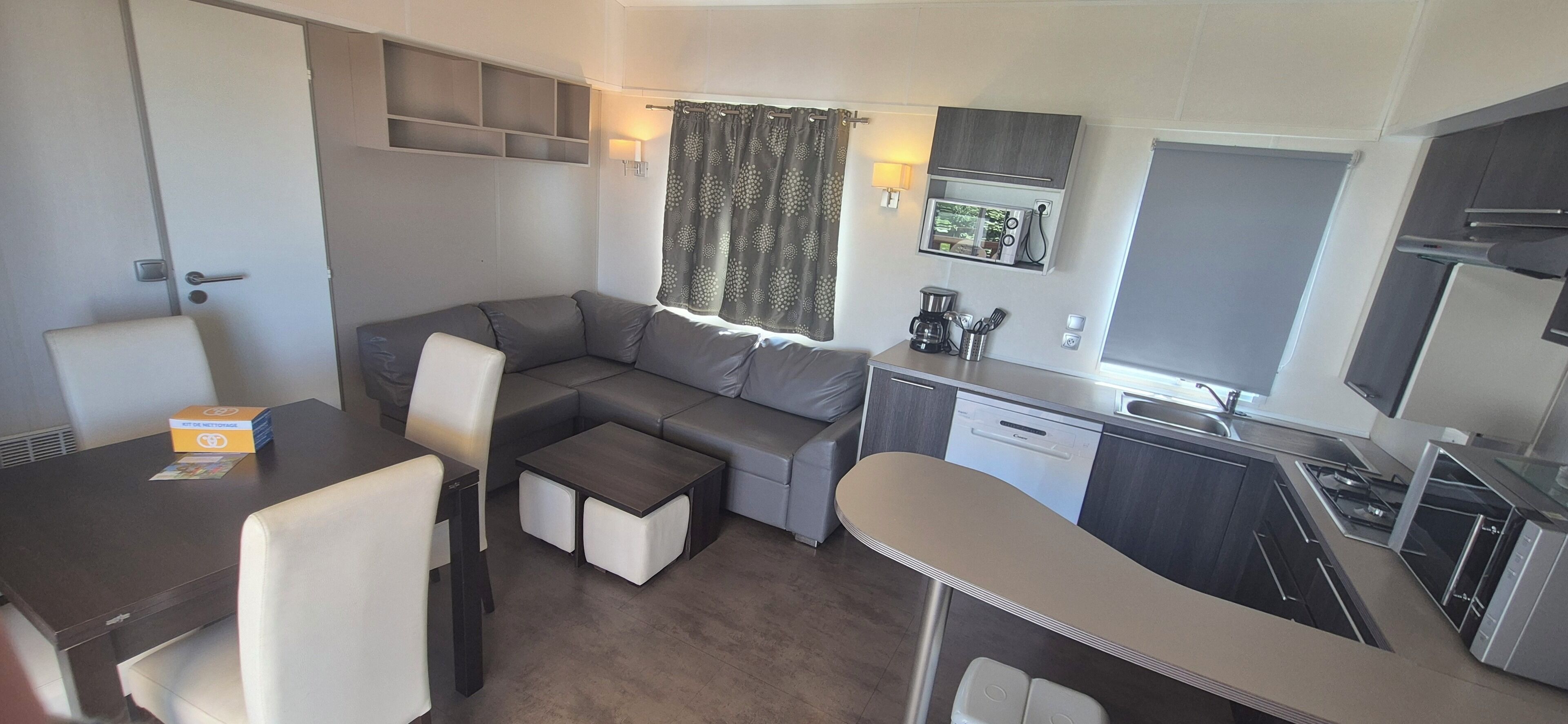 Un espace de vie compact comprenant un canapé, une table à manger, un coin cuisine avec un évier et une cuisinière, ainsi qu’une fenêtre avec des rideaux.
