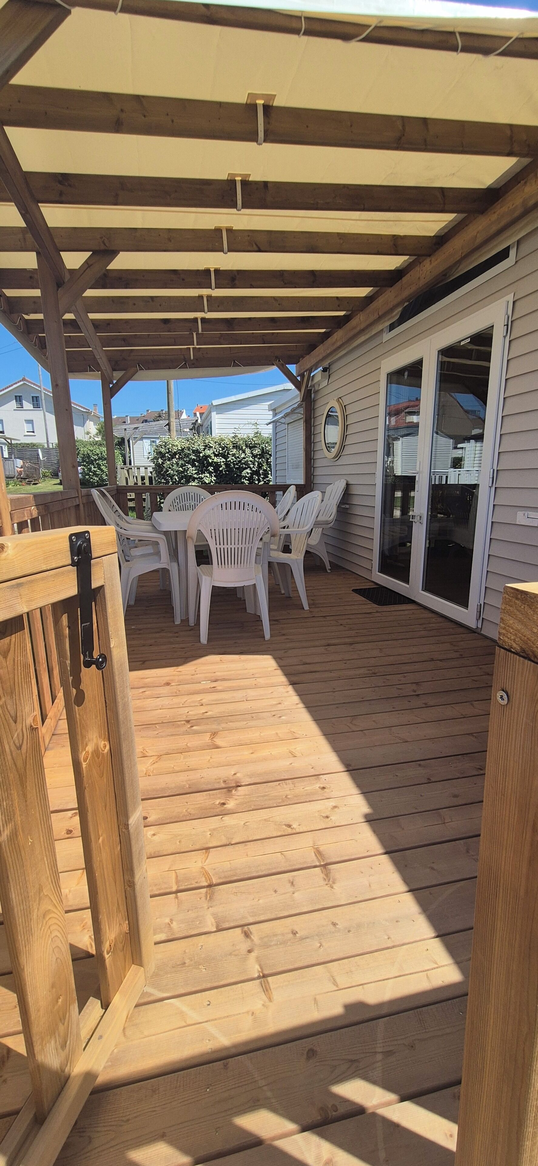 Une terrasse en bois avec une table et des chaises, un espace abrité et une porte-fenêtre coulissante.