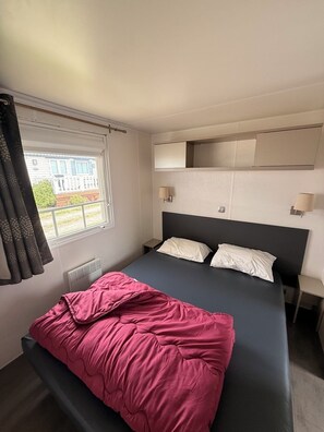 A bedroom with a bed, a window with curtains, a radiator, and a wall-mounted shelf. - Mobile home CONFORT le Portel plage chez Nono et Alex (Le Portel)