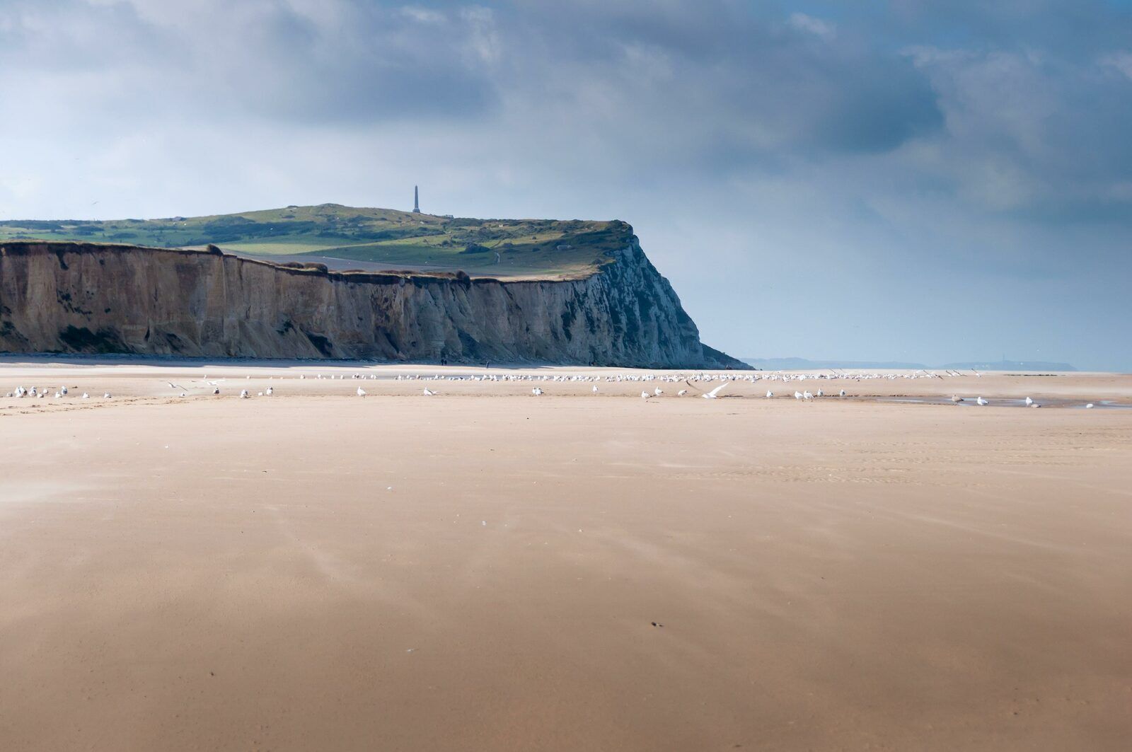 A coastal landscape with a sandy beach and a cliff.