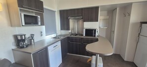 A compact kitchen with a microwave, stove, sink, and a small table. - Mobile home CONFORT le Portel plage chez Nono et Alex (Le Portel)