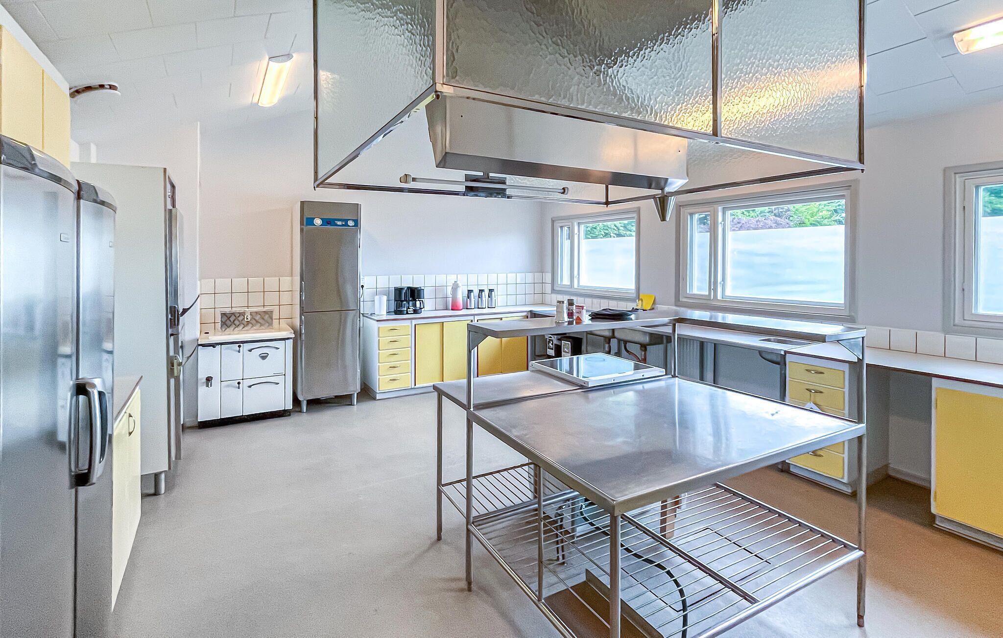 Une cuisine moderne dotée d’appareils électroménagers en acier inoxydable, d’un îlot central et offrant une vue sur l’extérieur grâce à de grandes fenêtres.