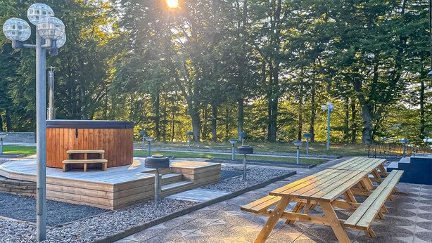 A wooden hot tub, picnic tables, and a stone-tiled deck in a park.