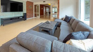 A modern living room with a large flat-screen TV, a sectional sofa, a coffee table, and a brick accent wall.