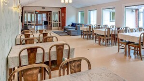 A spacious dining area with multiple tables and chairs, a sofa, and a chandelier.