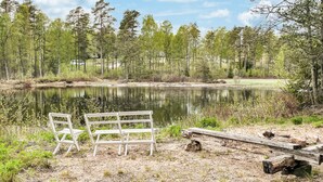 Rauhallinen paikka järven rannalla, jossa on puinen penkki ja piknikpöytä. Alue on vehreä, sillä sitä ympäröivät puut ja tyyni vesialue.