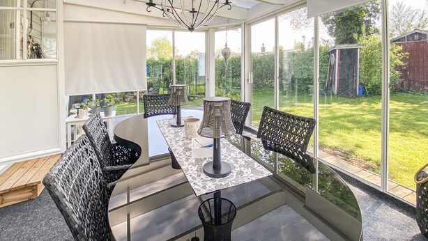 A conservatory with a table and chairs, large windows, and a chandelier.