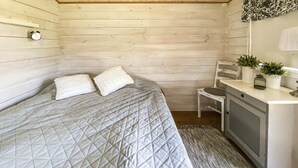 A bedroom with a bed, two pillows, a chair, a small desk, a clock, and a plant.