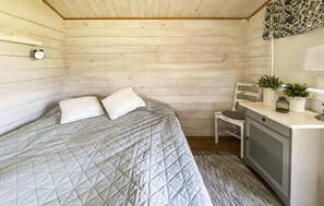 A bedroom with a bed, two pillows, a chair, a small desk, a clock, and a plant.