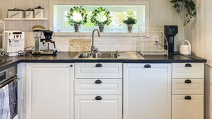 A kitchen with white cabinets, a stainless steel sink, a coffee maker, and two potted plants on the windowsill.