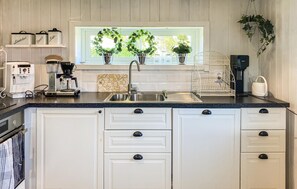 A kitchen with white cabinets, a stainless steel sink, a coffee maker, and two potted plants on the windowsill.