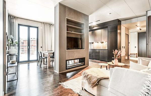 A modern living room with a fireplace, a dining area, and a kitchen.