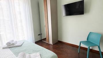 A hotel room with a bed, a TV mounted on the wall, a blue chair, and a wardrobe.