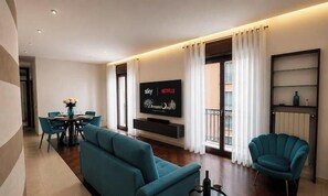 A modern living room with a sofa, chairs, a TV, and a dining area. - Dreamora Charme & Relax Salerno (Salerno)