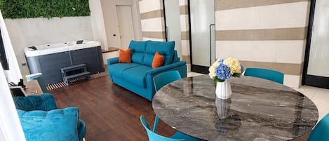 A modern living room with a round table, teal chairs, and a sofa with orange cushions.