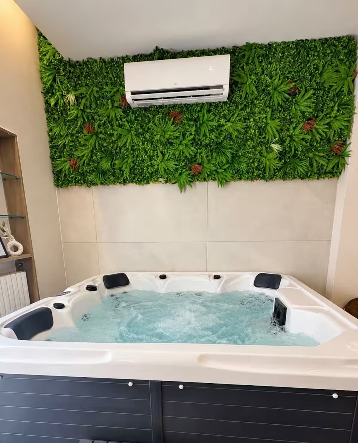 Un bain à remous rempli d’eau, un climatiseur fixé au mur et un mur végétal orné de feuillage.