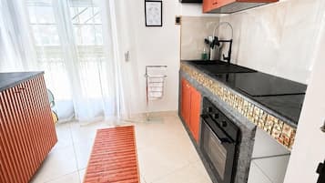 Una cocina moderna con horno empotrado, pileta y estufa. Posee piso de madera y un ventanal con cortinas traslúcidas.
