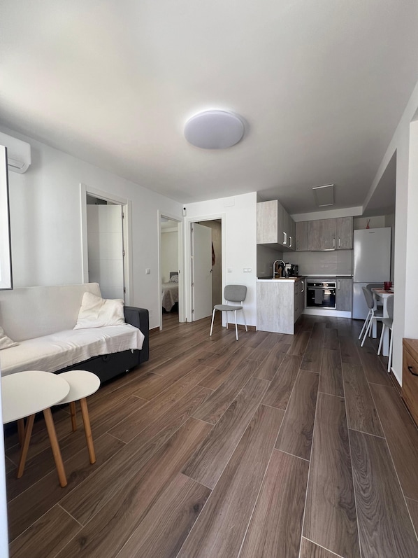 A modern living room with a sofa, a dining table, and a kitchen area with cabinets and appliances.