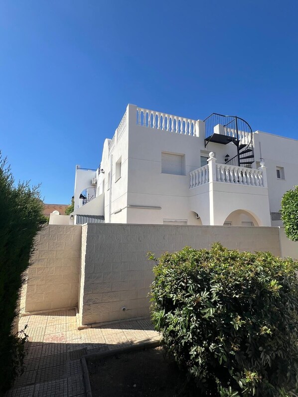 Un bâtiment blanc doté d’un escalier en colimaçon, d’un balcon et d’un mur en briques.