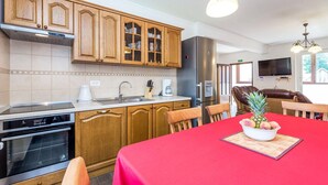 A modern kitchen with wooden cabinets, a stainless steel refrigerator, a coffee maker, and a dining area with a red tablecloth and a bowl of fruit. - 3 bedroom beautiful home in Jasenak (Jasenak)
