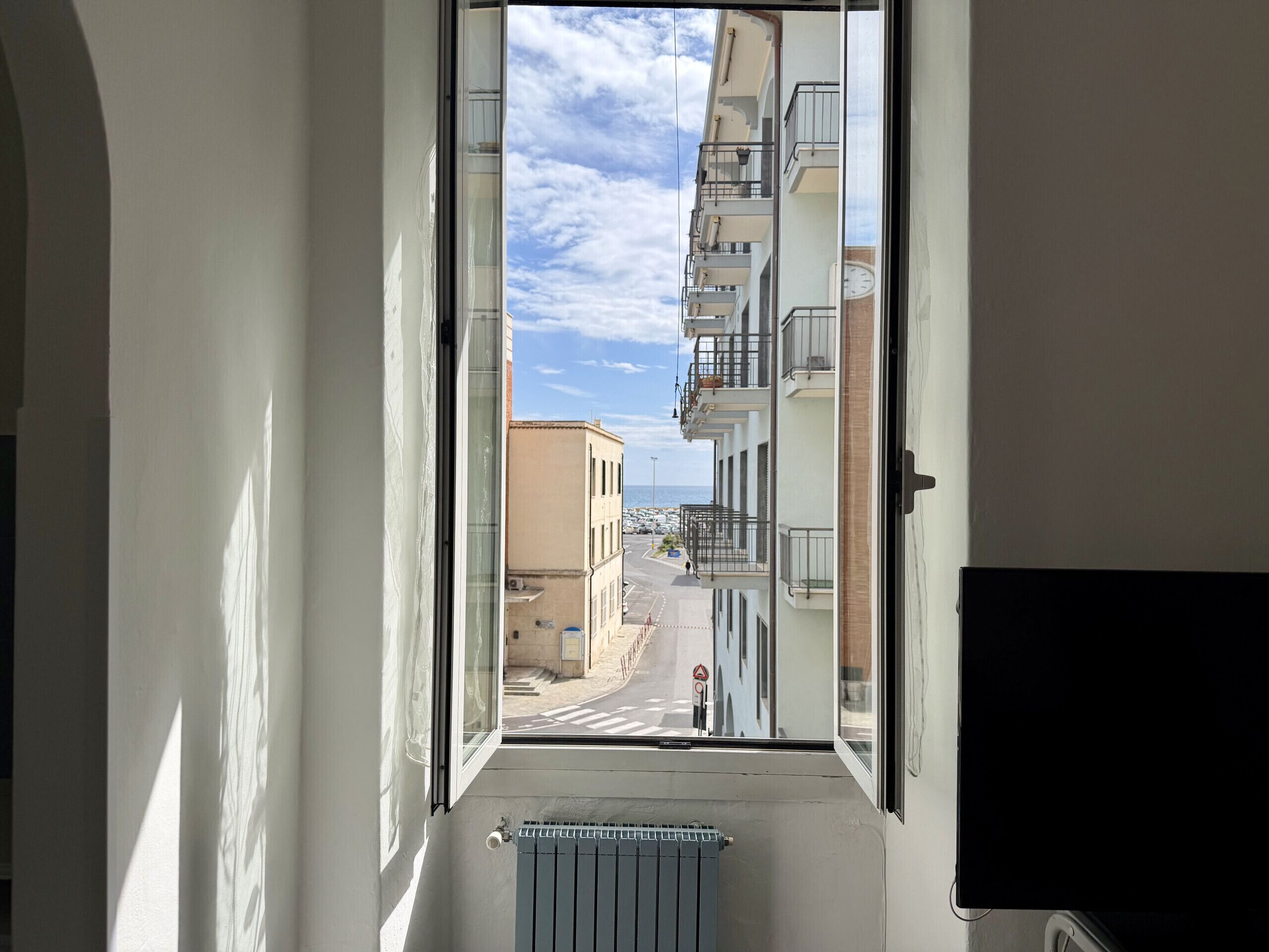Un pasillo estrecho con una ventana que da a la calle, un radiador y una puerta.