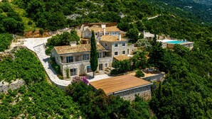 Ein großes, mehrgeschossiges Steinhaus mit Schwimmbecken, umgeben von dichtem Grün und Hügeln.