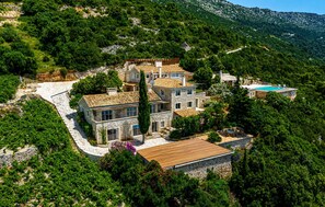A large, multi-story stone house with a swimming pool, surrounded by dense greenery and hills. - Luxurious home in Potomje (Potomje)