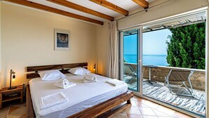 Ein Schlafzimmer mit Bett, Nachttisch, einem gerahmten Bild und einem Balkon mit Meerblick.