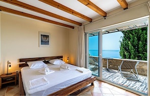 A bedroom with a bed, a nightstand, a framed picture, and a balcony with a view of the sea. - Luxurious home in Potomje (Potomje)