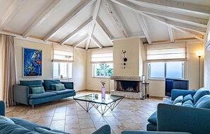A spacious living room with a high ceiling, a fireplace, and a large window. - Luxurious home in Potomje (Potomje)