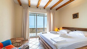 Ein Hotelzimmer mit Bett, Tisch, Stuhl und Meerblick durch eine Glastür.