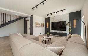 Ein modernes Wohnzimmer mit einer Sofagarnitur, einem Fernseher und einer Treppe.