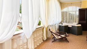 Ein Balkon mit weißen Vorhängen, einem Korbstuhl und einem kleinen Tisch mit Kissen.