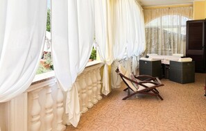 Ein Balkon mit weißen Vorhängen, einem Korbstuhl und einem kleinen Tisch mit Kissen.