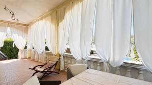 Ein Zimmer mit Balkon, weißen Vorhängen, einem Korbstuhl und einem Tisch.