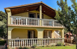 Ein zweistöckiges Gebäude mit Balkon, Schornstein und einem kleinen Garten.
