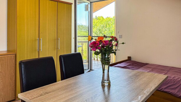 A room with a wooden table, two chairs, a bed, and a sliding glass door leading to a balcony with a view of greenery. - Awesome apartment in Medulin with WiFi (Medulin)