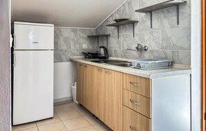 Eine kleine Küche mit einem weißen Kühlschrank, Holzschränken, einem Spülbecken und einer Arbeitsplatte mit Wasserkocher und Korb.