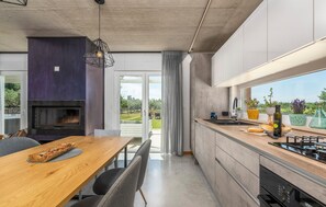 Eine moderne Küche mit Einbauofen, ein Essbereich mit Holztisch und -stühlen sowie ein Blick ins Freie durch große Fenster.