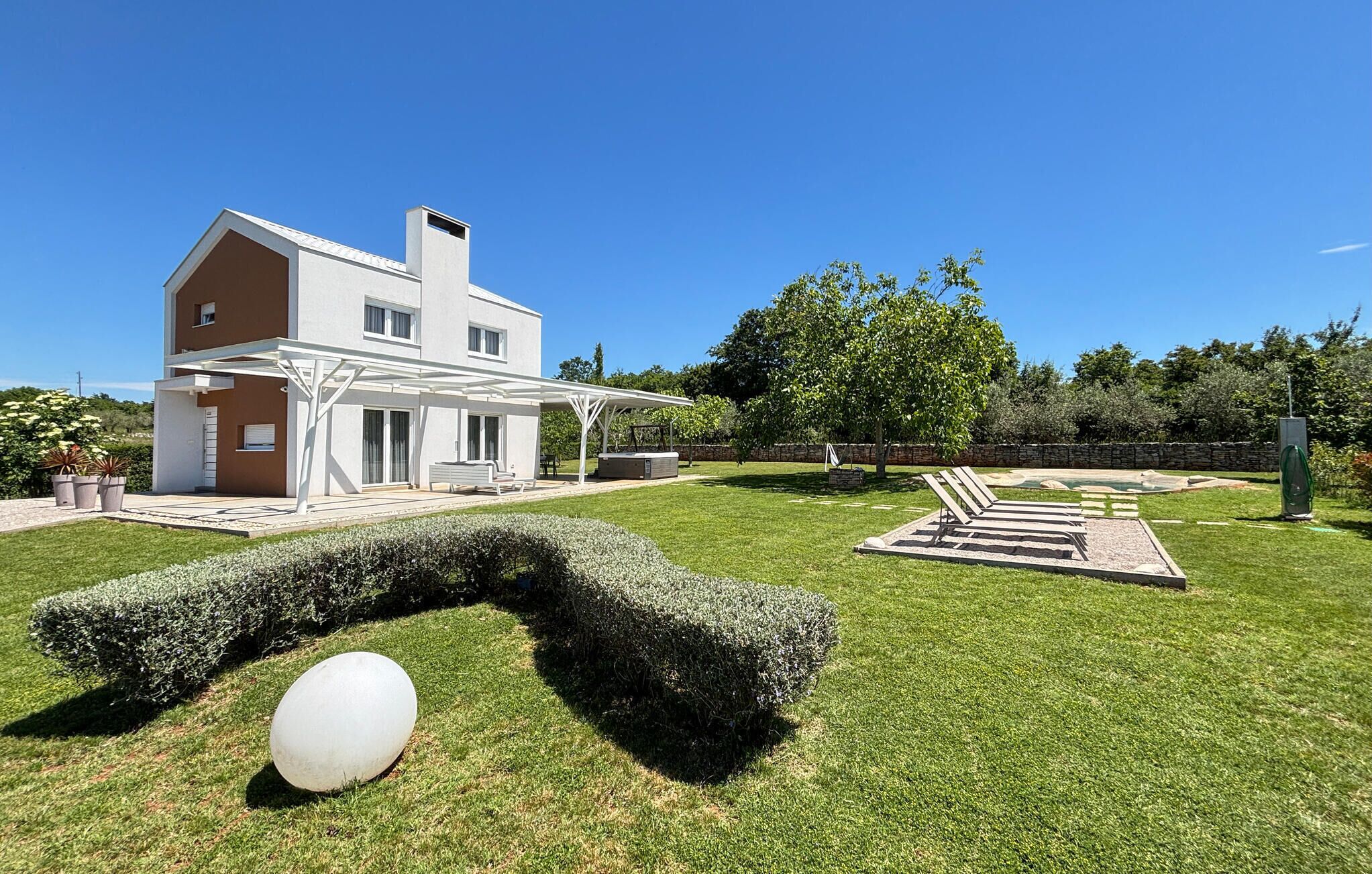 Una casa moderna de dos pisos con un porche cubierto, un césped cuidado y una gran escultura esférica.