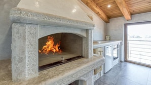 Una chimenea de piedra con fuego, una zona de cocina con armarios y un techo de madera.