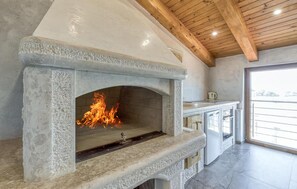 A stone fireplace with a fire, a kitchen area with cabinets, and a wooden ceiling. - Awesome apartment in Umag with WiFi (Umag)