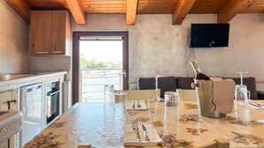 Una cocina con vigas de madera, un comedor con una mesa dispuesta para dos personas y un televisor montado en la pared.